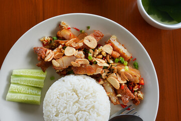 Delicious Thai fried pork with garlic served with steamed white rice, cucumber slices, and soup on wooden table, traditional Asian cuisine."