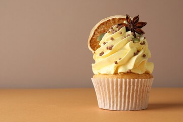Delicious cupcake with sprinkles and spices on coral table against grey background, closeup with space for text. Autumn atmosphere