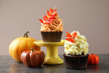 Delicious cupcakes with branches with red leaves and decorative pumpkins on grey textured table, closeup. Autumn atmosphere