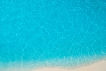 A tranquil, crystal-clear ocean surface with gentle waves meeting a sandy shore, creating a serene beach atmosphere.