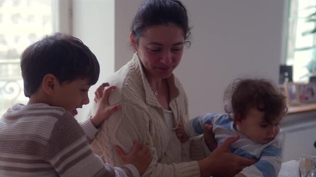 Mother holding baby while interacting with older child at dining table in bright family home interior