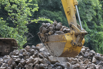 Powerful yellow excavator bucket efficiently scoops large pile of dark rocks at busy construction...