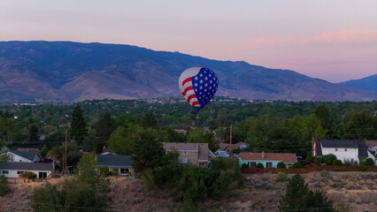 Aerial view of a patriotic hot air balloon drifts over the suburban landscape, with mountains in the backdrop, Reno, Nevada, United States.