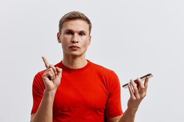 Young caucasian man in red shirt hold smartphone point finger use voice assistant digital...