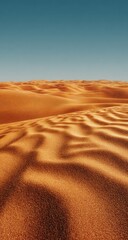 Undulating orange sand dunes stretch to a clear, deep blue sky, the texture of the sand emphasized by subtle shadows and light