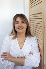 Woman in white blouse poses confidently with folded arms against wooden wall