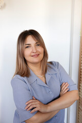 Woman with crossed arms smiles confidently in a light blue outfit against a simple background