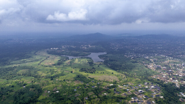Aerial view of a serene lake nestled among verdant forests and scattered dwellings under a vast, cloudy sky, Osogbo, Osun, Nigeria.
