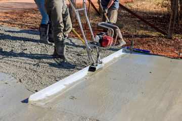 Crew members are laying down fresh concrete for sidewalk on work day, ensuring smooth finish.