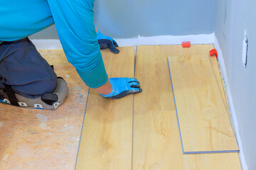 Craftsman lays down laminate flooring planks in simple living space, focusing on precision detail.