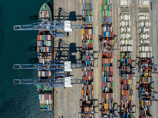 Aerial view of a cargo ship berthed at the Port of Piraeus, a vibrant tableau of stacked containers casting long shadows on the concrete, Piraeus, Greece.
