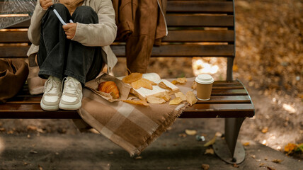 Autumn picnic scene with coffee, croissant, and a book on a park bench.