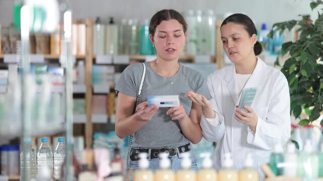 Attentive young girl buyer choosing medical ointment and professional asian female parmacist helping in small pharmacy