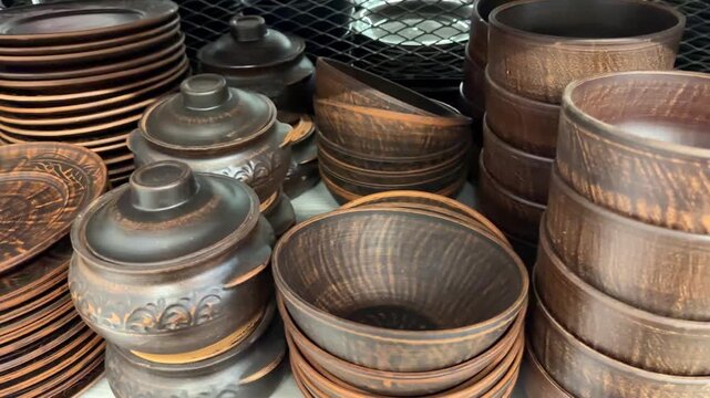 Handmade earthenware and traditional ceramic tableware collection. Including rustic brown plates. Bowls. And pots. Displayed for sale on store shelves. Highlighting authentic craft and pottery skills