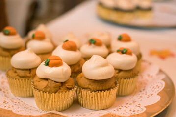 Fall pumpkin cupcakes with cream cheese frosting and pumpkin decorations sitting on a dessert table