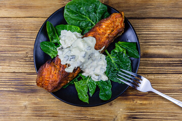 Plate with roasted salmon steak, tartar sauce and spinach leaves on a wooden table. Top view