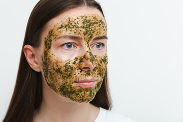 Portrait of young girl or woman with green natural homemade cosmetic mask on her face with white background. Concept of self-care at home or in salon. Close up