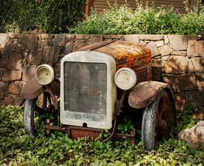 front end of a rusty old car against a stone wall