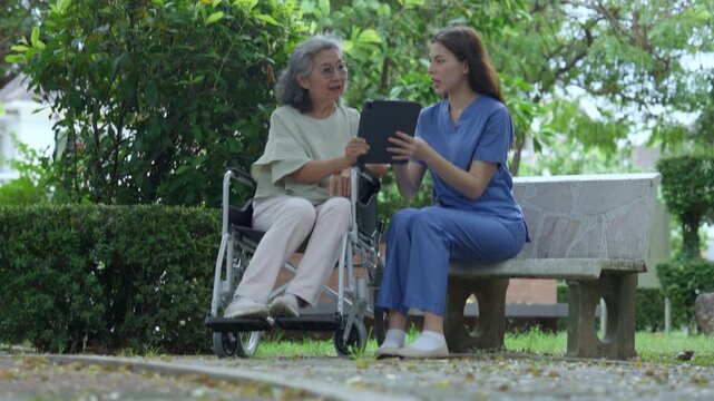 A caregiver is monitoring the condition of an elderly Asian woman after she is discharged from the hospital online using a tablet to access treatment information from her doctor.