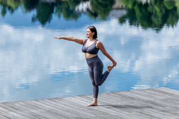Young caucasian female practicing yoga pose on lakeside dock in nature