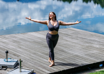 Fototapeta premium Young caucasian female practicing yoga outdoors on lakeside dock