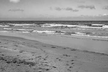 Waves gently lap against the shore on a cloudy beach with footprints in the sand