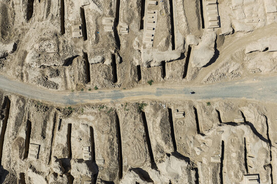 Aerial view of ancient graves, with their stark geometric forms etched into the ochre earth, bisected by a pale road, Cemetery in Turpan, Xinjiang, China.
