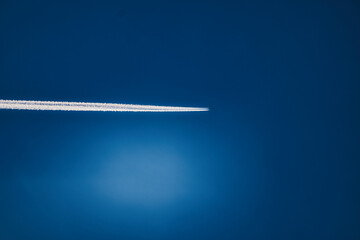 Airplane flying high in blue sky leaving white contrail trail behind