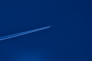 Airplane flying high in blue sky leaving white contrail trail behind
