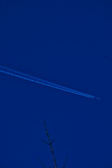 Airplane flying high in blue sky leaving white contrail trail behind