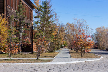 A sidewalk flanked by autumn trees beside a wooden house. The area of the Old Town in Yakutsk