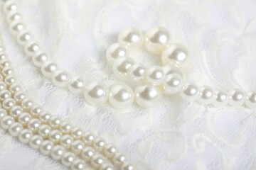 Beautiful lace fabric and pearls on white background, closeup