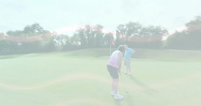 Female golfer aligning putter and swinging ball toward hole to win with partner handling flagstick