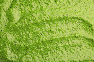Tasty green pesto sauce as background, top view