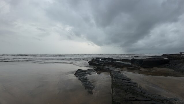Moody and tranquil landscape of an evening beach, with a rocky shore and calm, misty ocean.
