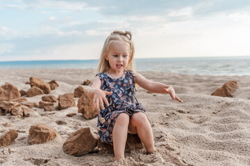 A little child girl in a dress walks on the sand on the beach in the summer evening