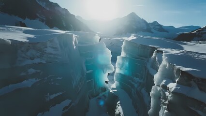 Aerial view of a deep glacial crevasse with turquoise ice and snow-covered mountains in the background