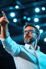 A man in a white shirt gestures passionately while speaking, illuminated by blue stage lights, conveying confidence and engagement.