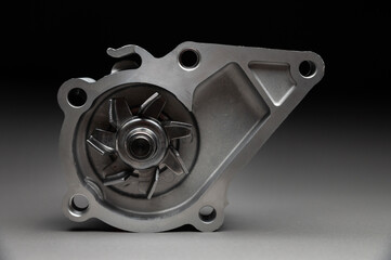Obraz premium A new car part on a gradient gray background. Close-up of a new internal combustion engine coolant pump. Contrast backlighting.