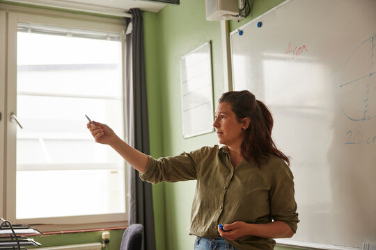 Female professor holding felt tip pen pointing while standing near whiteboard in classroom