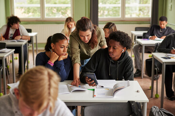 Female teacher assisting junior high students using calculator for math problem in classroom at school