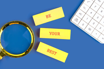 Copy space. Business concept. BE YOUR BEST made of wooden blocks on blue background next to calculator, top view