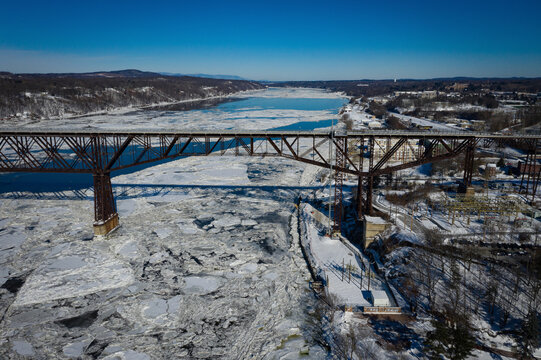 Aerial view of the Rip Van Winkle Bridge cutting across the icy, frozen Hudson River under a clear winter sky, Hudson, New York, United States.