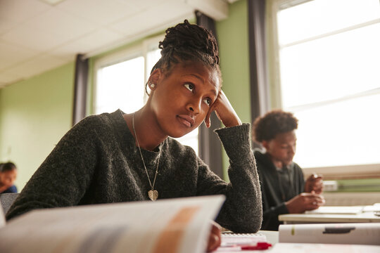 Low angle view of teenage female student with hair bun leaning on elbow at desk in classroom