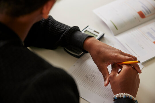 Over the shoulder view of teenage boy holding pencil solving math equation on paper in school