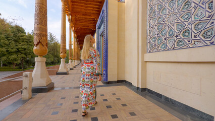 Woman in Uzbek patterned attire admiring traditional architecture in Tashkent