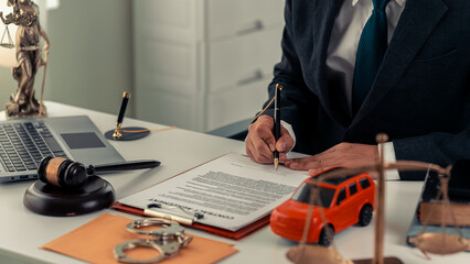 A small red toy car sits next to a judge's gavel on a table in a lawyer's office. Car accident concept. Law. Close-up of