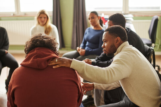 Male mental health professional consoling sad teenage boy during group therapy session in school