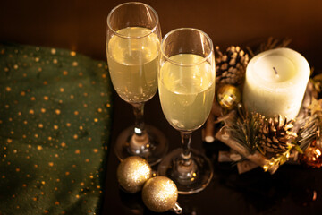 Two champagne glasses with bubbles, decorative candle, pine cones, golden baubles and green fabric with stars. Warm festive composition for Christmas and New Year cards, invitations and sales.