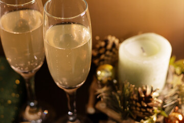 Two champagne glasses with bubbles, decorative candle, pine cones, golden baubles and green fabric with stars. Warm festive composition for Christmas and New Year cards, invitations and sales.